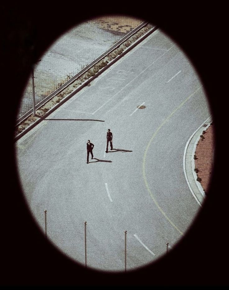 Two figures standing apart on an empty road, seen from high above.